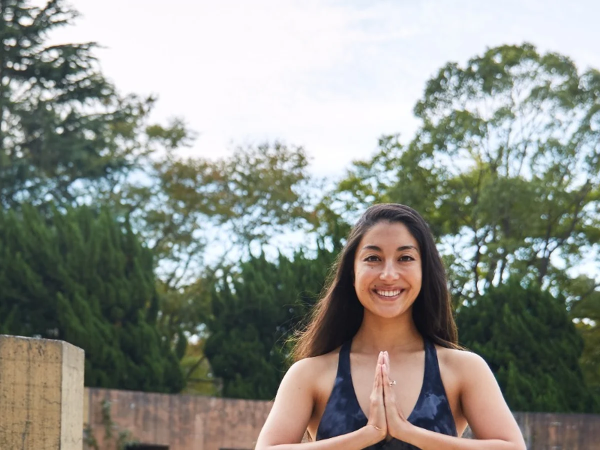 Miné smiling outdoors with her hands in prayer